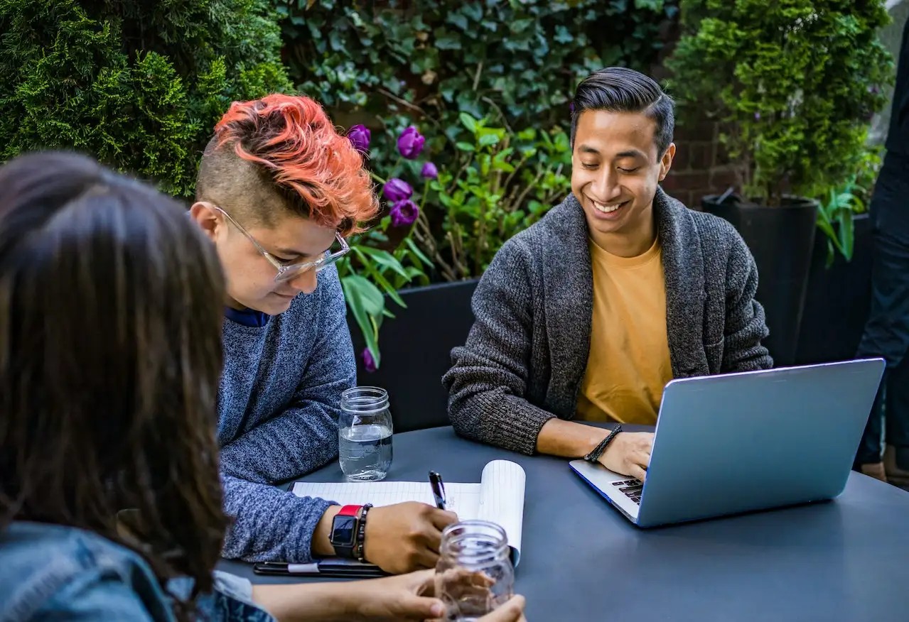 Man in Orange Crew-neck Shirt Using Laptop Beside Two People