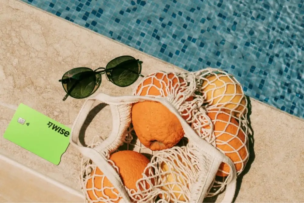 Wise debit card, sunglasses and oranges by the pool